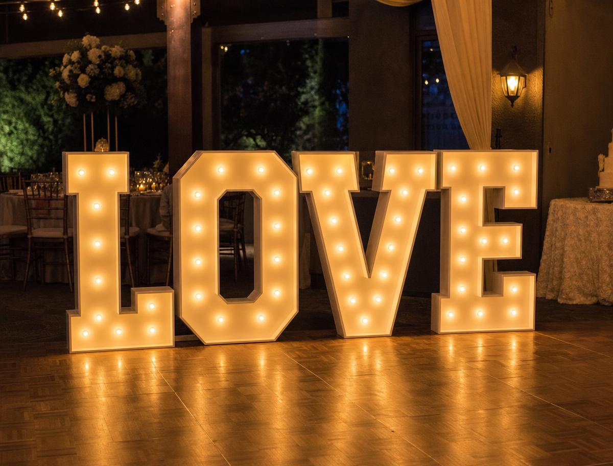 Giant marquee bulb letters spelling LOVE on a wedding dance floor