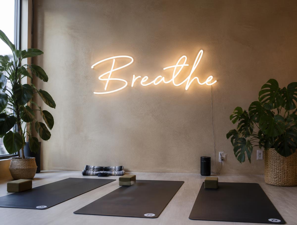 Soft white Breathe LED neon sign on a studio wall above yoga mats