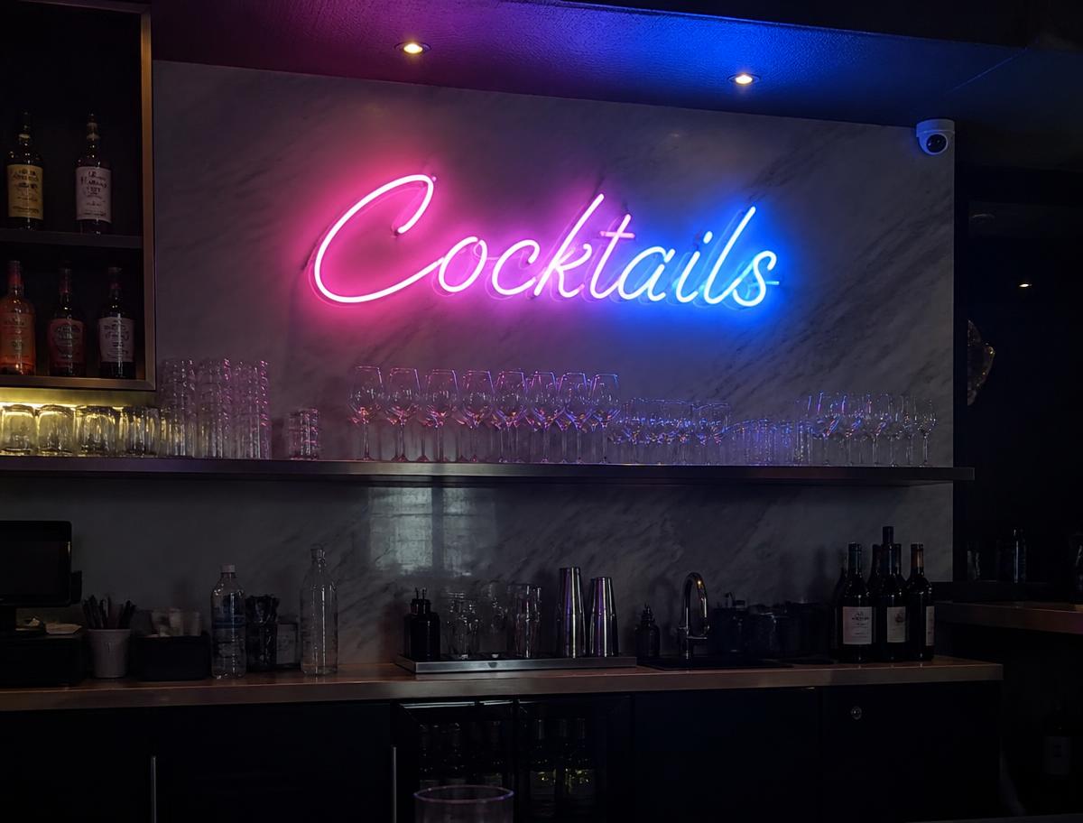 Pink Cocktails LED neon script sign behind a bar with glassware